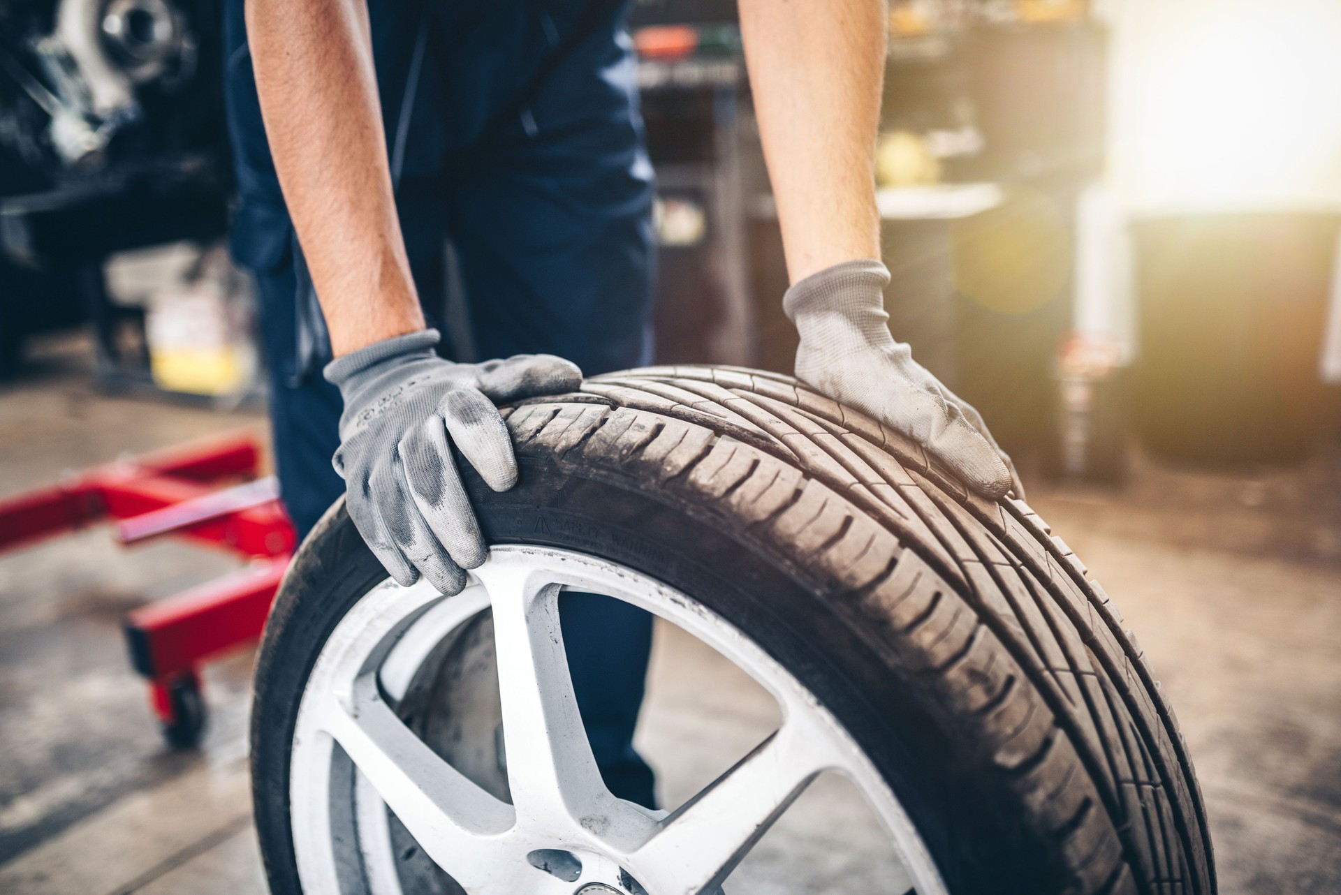 Car tire shop and service - mechanic holding a tyre.